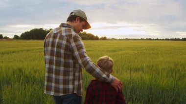 Çiftçi ve oğlu günbatımı tarımının önünde. Kırsalda bir adam ve bir çocuk. Babalık kavramı, köy hayatı, tarım ve kırsal yaşam tarzı..
