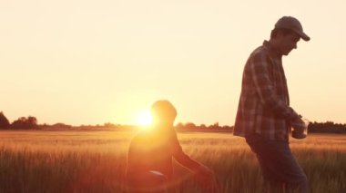 Farmer and his son in front of a sunset agricultural landscape. Man and a boy in a countryside field. The concept of fatherhood, country life, farming and country lifestyle.