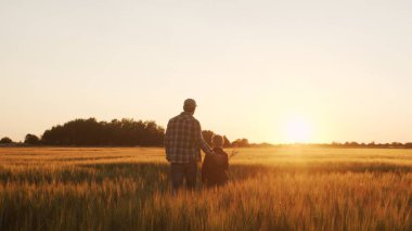 Farmer and his son in front of a sunset agricultural landscape. Man and a boy in a countryside field. The concept of fatherhood, country life, farming and country lifestyle.