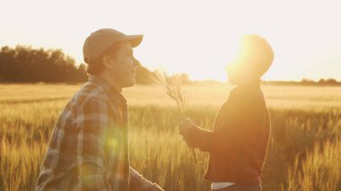 Çiftçi ve oğlu günbatımı tarımının önünde. Kırsalda bir adam ve bir çocuk. Babalık kavramı, köy hayatı, tarım ve kırsal yaşam tarzı..