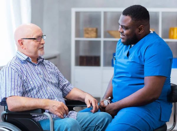 Professional doctor helps an elderly man with chronic diseases. Therapist and patient in home interior. The concept of health care and medicine.