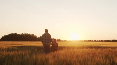 Farmer and his son in front of a sunset agricultural landscape. Man and a boy in a countryside field. The concept of fatherhood, country life, farming and country lifestyle.