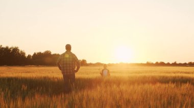Farmer and his son in front of a sunset agricultural landscape. Man and a boy in a countryside field. The concept of fatherhood, country life, farming and country lifestyle.