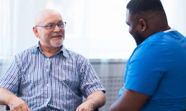 Professional doctor helps an elderly man with chronic diseases. Therapist and patient in home interior. The concept of health care and medicine.