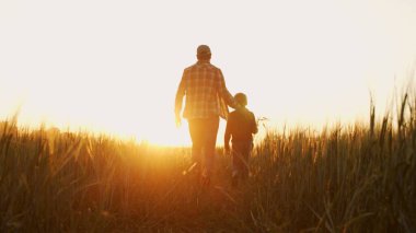 Farmer and his son in front of a sunset agricultural landscape. Man and a boy in a countryside field. The concept of fatherhood, country life, farming and country lifestyle.