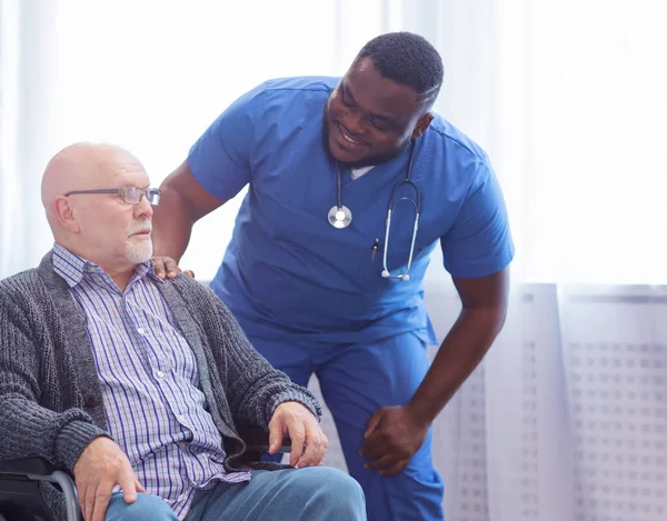 Professional doctor helps an elderly man with chronic diseases. Therapist and patient in home interior. The concept of health care and medicine.