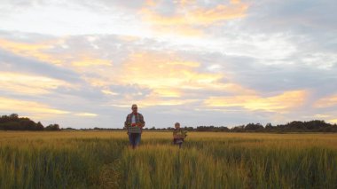 Çiftçi ve oğlu günbatımı tarımının önünde. Kırsalda bir adam ve bir çocuk. Babalık kavramı, köy hayatı, tarım ve kırsal yaşam tarzı..