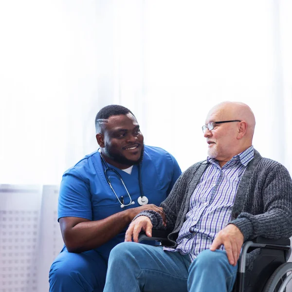 Professional doctor helps an elderly man with chronic diseases. Therapist and patient in home interior. The concept of health care and medicine.