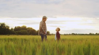 Farmer and his son in front of a sunset agricultural landscape. Man and a boy in a countryside field. The concept of fatherhood, country life, farming and country lifestyle.