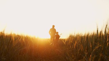 Çiftçi ve oğlu günbatımı tarımının önünde. Kırsalda bir adam ve bir çocuk. Babalık kavramı, köy hayatı, tarım ve kırsal yaşam tarzı..