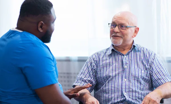 Professional doctor helps an elderly man with chronic diseases. Therapist and patient in home interior. The concept of health care and medicine.