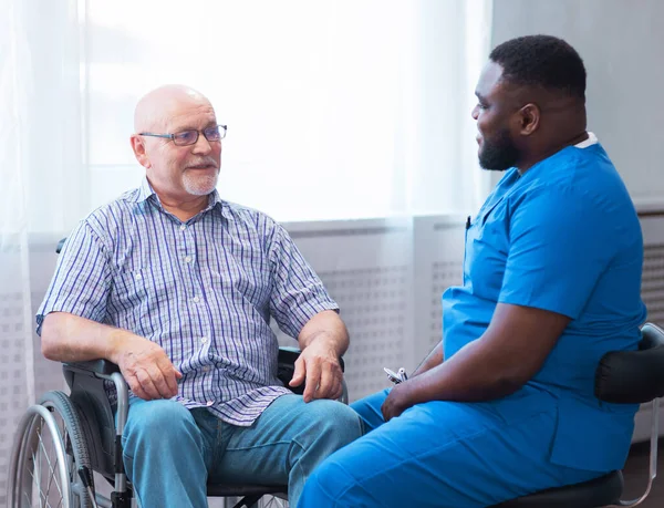 Professional doctor helps an elderly man with chronic diseases. Therapist and patient in home interior. The concept of health care and medicine.