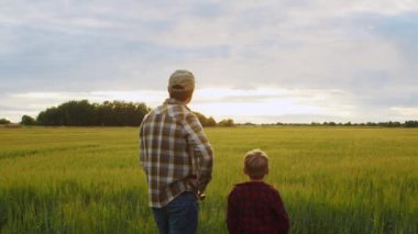 Farmer and his son in front of a sunset agricultural landscape. Man and a boy in a countryside field. The concept of fatherhood, country life, farming and country lifestyle.