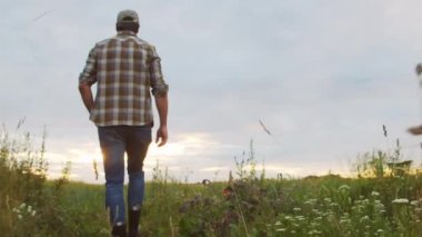 Farmer walking on field against sunset agricultural landscape. Man in a countryside field. The concept of ecology, food production, farming and country lifestyle.