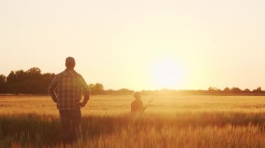 Farmer and his son in front of a sunset agricultural landscape. Man and a boy in a countryside field. The concept of fatherhood, country life, farming and country lifestyle.