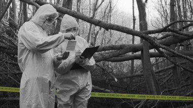 Detectives are collecting evidence in a crime scene. Forensic specialists are making expertise. Professional police investigation in a forest. Black and white image with yellow police line.