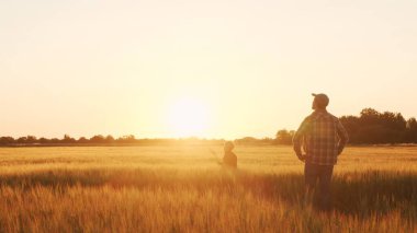 Farmer and his son in front of a sunset agricultural landscape. Man and a boy in a countryside field. The concept of fatherhood, country life, farming and country lifestyle.