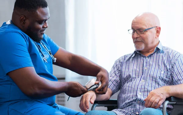 Professional doctor helps an elderly man with chronic diseases. Therapist and patient in home interior. The concept of health care and medicine.