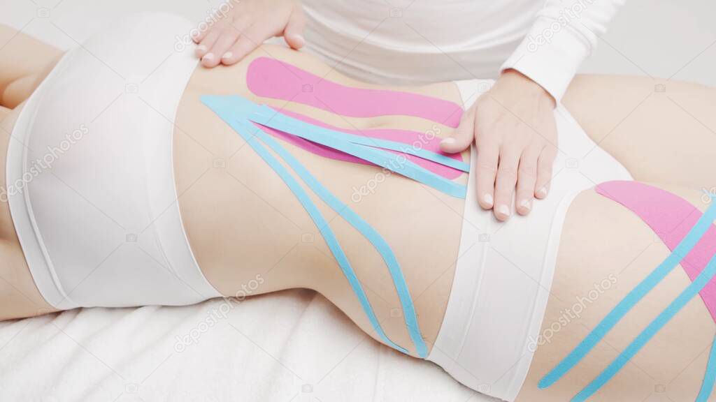 Therapist is applying tape to beautiful female body. Physiotherapy, kinesiology and recovery treatment.