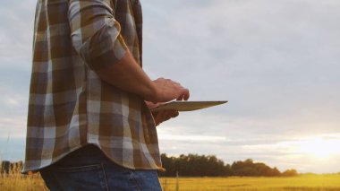 Günbatımı tarım manzarasının önünde tablet bilgisayarlı bir çiftçi. Kırsal kesimde bir adam. Kır hayatı, gıda üretimi, tarım ve teknoloji kavramı.