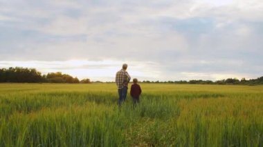 Farmer and his son in front of a sunset agricultural landscape. Man and a boy in a countryside field. The concept of fatherhood, country life, farming and country lifestyle.