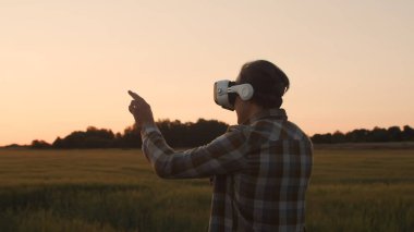 Sanal gerçeklik kaskı takan çiftçi, gün batımı tarımının önünde. Kırsal kesimde bir adam. Kır hayatı, gıda üretimi, tarım ve teknoloji kavramı.