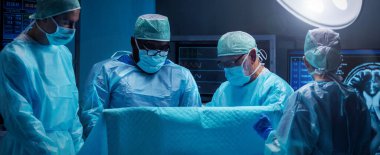 Diverse team of professional medical surgeons perform surgery in the operating room using high-tech equipment. Doctors work to save a patient in a modern hospital. The concept of medicine, technology