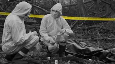 Detectives are collecting evidence in a crime scene. Forensic specialists are making expertise. Professional police investigation in a forest. Black and white image with yellow police line.