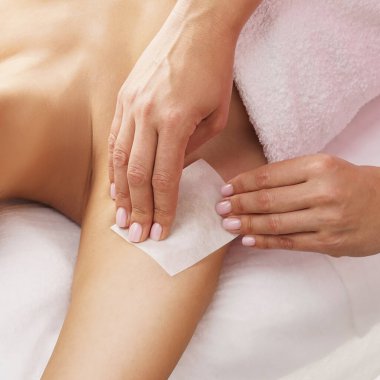 Güzellik uzmanı, genç ve güzel kadın koltukaltlarındaki kılları sıcak balmumuyla alıyor. Kızın güzellik tedavi prosedürü var. Defilasyon, epilasyon, cilt ve sağlık konseptleri.