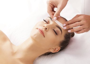 Profesyonel işçi, genç ve güzel kadın yüzünden sıcak balmumuyla saç kesiyor. Kızın güzellik tedavi prosedürü var. Defilasyon, epilasyon, cilt ve sağlık konseptleri.