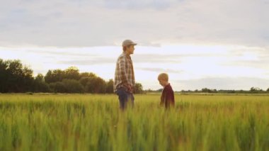 Çiftçi ve oğlu günbatımı tarımının önünde. Kırsalda bir adam ve bir çocuk. Babalık kavramı, köy hayatı, tarım ve kırsal yaşam tarzı..