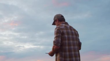 Günbatımı tarımının önündeki çiftçi. Kırsal kesimde bir adam. Kır hayatı, gıda üretimi, tarım ve kırsal yaşam tarzı kavramı.