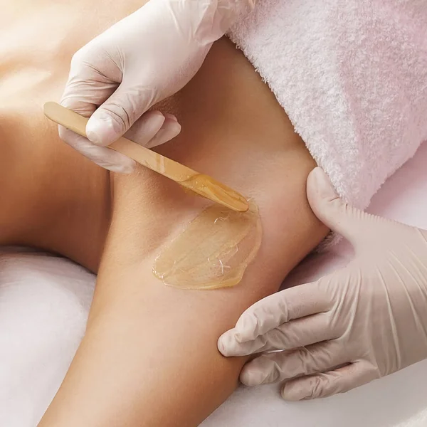 The concept of hair removal, beauty and health. A young girl is getting an epilation procedure. A processional beauty worker is making depilation with hot wax.