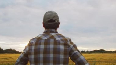 Günbatımı tarımının önündeki çiftçi. Kırsal kesimde bir adam. Kır hayatı, gıda üretimi, tarım ve kırsal yaşam tarzı kavramı.