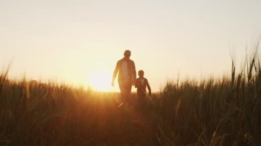 Farmer and his son in front of a sunset agricultural landscape. Man and a boy in a countryside field. The concept of fatherhood, country life, farming and country lifestyle.
