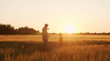 Farmer and his son in front of a sunset agricultural landscape. Man and a boy in a countryside field. The concept of fatherhood, country life, farming and country lifestyle.