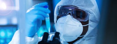Koruyucu kıyafetli profesyonel Afro-Amerikan doktor modern bir laboratuvarda bilimsel deneyler yapıyor ve aşı geliştiriyor. Laboratuvar asistanı iş yerinde. Bilim ve tıp kavramı.