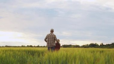 Farmer and his son in front of a sunset agricultural landscape. Man and a boy in a countryside field. The concept of fatherhood, country life, farming and country lifestyle.