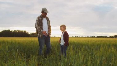 Çiftçi ve oğlu günbatımı tarımının önünde. Kırsalda bir adam ve bir çocuk. Babalık kavramı, köy hayatı, tarım ve kırsal yaşam tarzı..