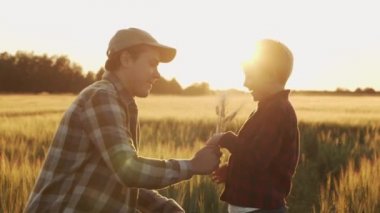 Farmer and his son in front of a sunset agricultural landscape. Man and a boy in a countryside field. The concept of fatherhood, country life, farming and country lifestyle.