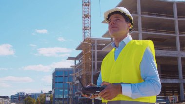 İnşaat alanının önünde duran profesyonel müteahhit. Kasklı ve yelekli ustabaşı. Ofis binası ve vinç arka planı. İş, gayrimenkul ve yatırım kavramları.