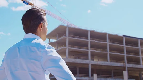 Business person standing in front of construction site. Office building and crane background. Development, real estate and investment concepts.