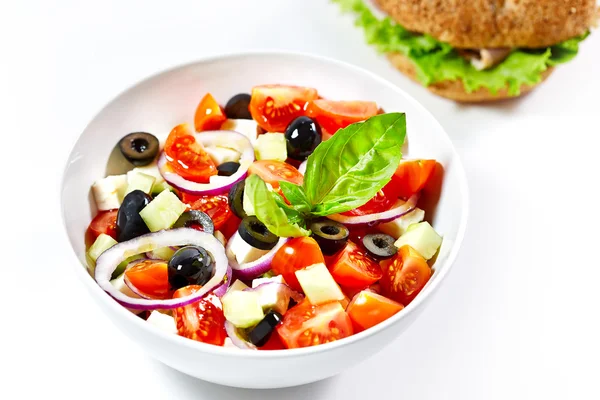 Light greek salad with fresh vegetables and burger in the backgr — Stock Photo, Image