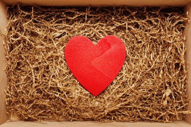 Present box with big red heart lying on brown shredded craft paper filler, top view from above, Valentine day concept