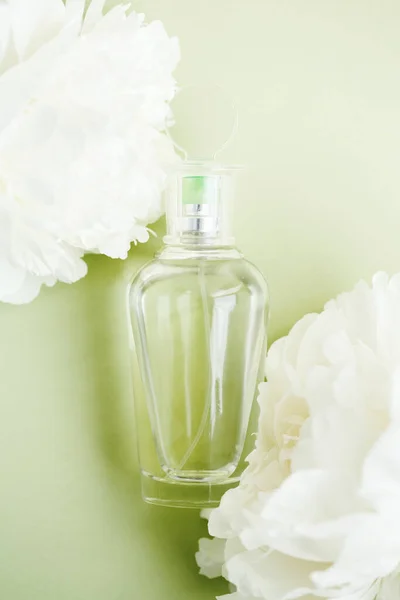 透明造型玻璃瓶与香水之间的新鲜的白色牡丹花浅绿色的石灰色 顶部视图 — 图库照片