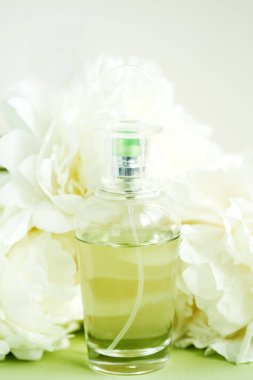 Parfümlü taklit cam şişe açık yeşil pastel renkte taze beyaz şakayık çiçekleri arasında.