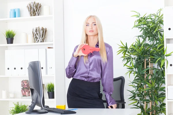 Die junge Frau im Büro hält einen großen roten Schlüssel in der Hand — Stockfoto