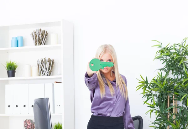 Mladá žena v kanceláři leží velký zelený klíč — Stock fotografie