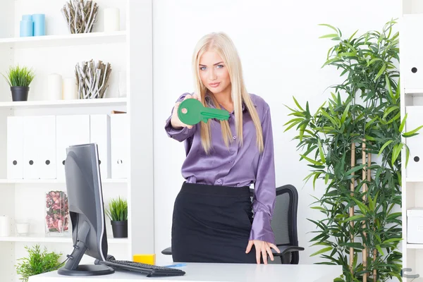 Die junge Frau im Büro hält einen großen grünen Schlüssel in der Hand — Stockfoto