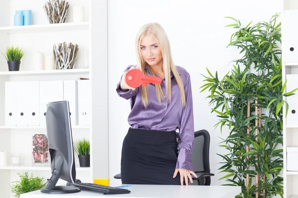 Die junge Frau im Büro hält einen großen roten Schlüssel in der Hand — Stockfoto